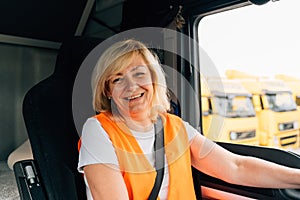 Mature woman truck driver steering wheel inside lorry cabin. Happy middle age female trucker portrait