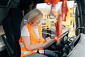 Mature woman truck driver steering wheel inside lorry cabin. Happy middle age female trucker portrait