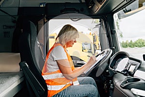 Mature woman truck driver steering wheel inside lorry cabin. Happy middle age female trucker portrait