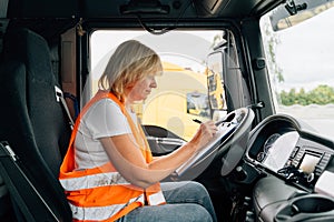 Mature woman truck driver steering wheel inside lorry cabin. Happy middle age female trucker portrait