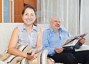 Mature woman with TV remote against man with newspaper