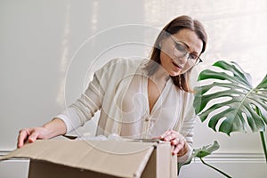 Mature woman unpacks cardboard box on table at home, in office photo