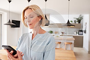 Mature Woman Using App On Mobile Phone To Control Central Heating Temperature In House photo