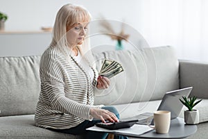 Mature woman using calculator and holding money