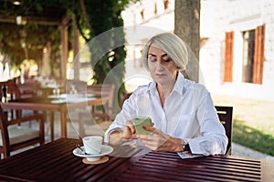 Mature woman using mobile phone while sitting at a cafe and drinking coffee