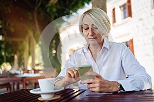 Mature woman using mobile phone while sitting at a cafe and drinking coffee