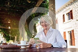 Mature woman using mobile phone while sitting at a cafe and drinking coffee