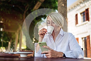 Mature woman using mobile phone while sitting at a cafe and drinking coffee