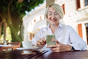 Mature woman using mobile phone while sitting at a cafe and drinking coffee