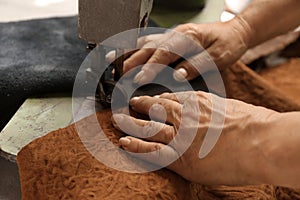 Mature woman using sewing machine in leather workshop, closeup