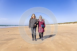 A mature woman walking with her elderly mother by the beach at autumn