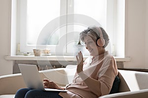 Mature woman wear headphones enjoy communication use laptop and videoconference photo