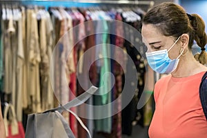 Mature woman wearing face protective mask buying at a clothes shop, indoors