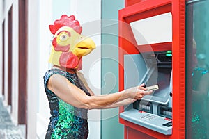 Mature woman wearing mask withdraw money from bank cash machine with debit card - Surreal image of half human and animal