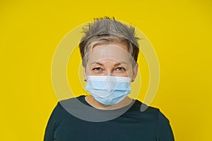 Mature woman wearing medical face mask with happy eyes smiling looking at camera wearing green blouse isolated on yellow