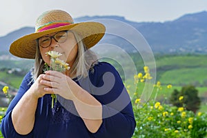 mature woman with white hair and hat holding a bouquet of daisies in her hands