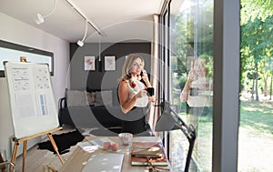 Mature woman working indoors in home office in container house in backyard.