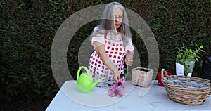 Mature woman working on a worktable in the garden of a house against a green bush in the background