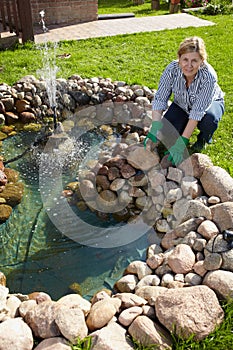 Mature woman works around pond in her garden