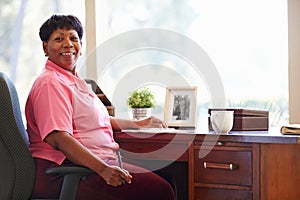 Mature Woman Writing In Notebook Sitting At Desk