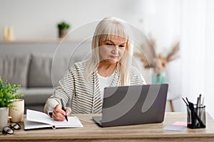 Mature woman writing and using pc laptop at home