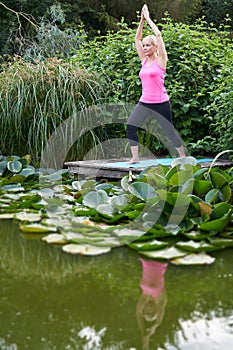 Mature Woman In Yoga Position On Wooden Jetty By Lake