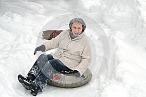 Mature woman young at heart. Happy smiling elderly female riding on snow tubing. Senior lady sledding slide down hill. Winter fun
