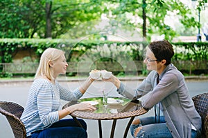 Mature women friends celebrating meeting clinking tea cups in outdoor cafe