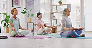 Mature women meditating in lotus pose with mudra hand gesture during a fitness class in a yoga studio. Calm, relaxed and