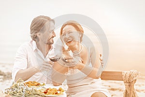 Mature woman and man happy together. Loving couple look each other embracing and drink red wine dating at beach cafe