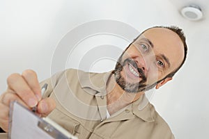 mature worker in beige uniform writing on clipboard