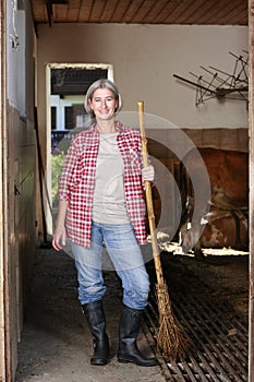 Matured farm woman sweeping the stable