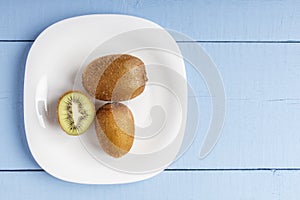 Matured kiwi fruits on white plate and on wooden table for vegetarian food. Top view. Copy space