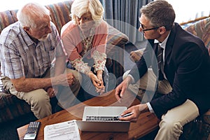 Matured male physician and senior couple discussing over laptop at retirement home