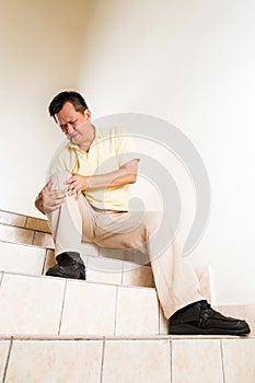 Matured man suffering acute knee joint pain seated on stairs