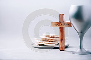 Matzos unleavened bread, chalice of wine, wooden cross on grey background. Christian communion for reminder of Jesus sacrifice.