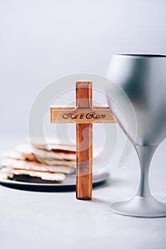 Matzos unleavened bread, chalice of wine, wooden cross on grey background. Christian communion for reminder of Jesus sacrifice.