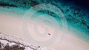 Maumere - A drone shot of a couple sitting on a white sand beach
