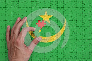 Mauritania flag is depicted on a puzzle, which the man`s hand completes to fold