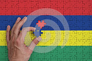 Mauritius flag is depicted on a puzzle, which the man`s hand completes to fold