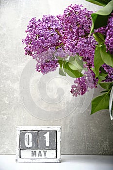 May 01 on calendar and bouquet of blooming lilac on gray background.