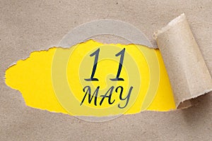 May 11. 11th day of the month, calendar date. Hole in paper with edges torn off. Yellow background is visible through ragged hole.