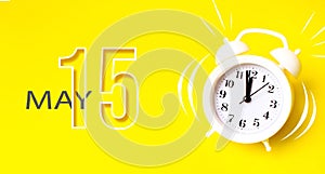May 15th. Day 15 of month, Calendar date. White alarm clock with calendar day on yellow background. Minimalistic concept of time,