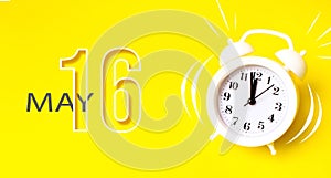 May 16th. Day 16 of month, Calendar date. White alarm clock with calendar day on yellow background. Minimalistic concept of time,