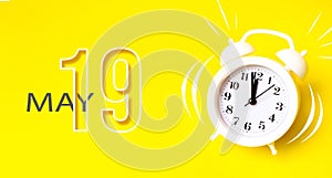 May 19th. Day 19 of month, Calendar date. White alarm clock with calendar day on yellow background. Minimalistic concept of time,