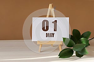 May 1st. Day 1 of month, Calendar date. Green branch, easel with the date and month on desktop. Close-up, brown