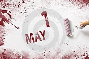 May 1st . Day 1 of month, Calendar date. The hand holds a roller with red paint and writes a calendar date on a white background.