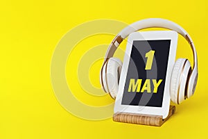 May 1st . Day 1 of month, Calendar date. Stylish headphones and modern tablet on yellow background. Space for text. Concept