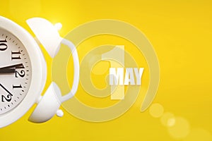 May 1st . Day 1 of month, Calendar date. White alarm clock on yellow background with calendar day. Spring month, day of the year