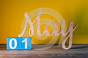 May 1st. Day 1 of month, wooden carved calendar on yellow background. Spring time concept